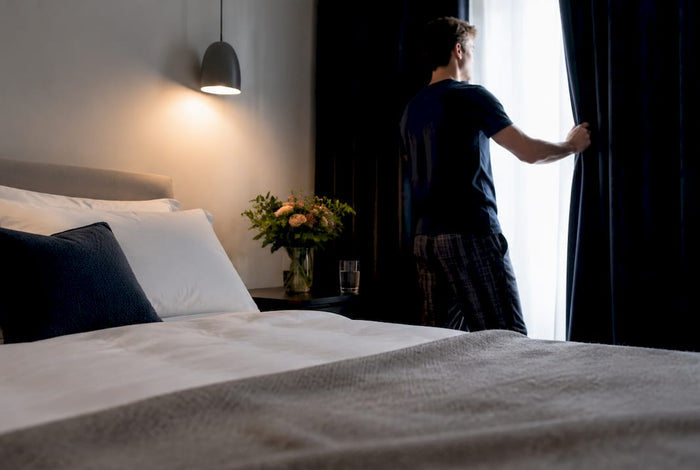 Man adjusting curtains in bedroom for sleep