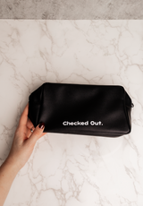 Black pouch with 'Checked Out.' text held by a hand on a marble surface